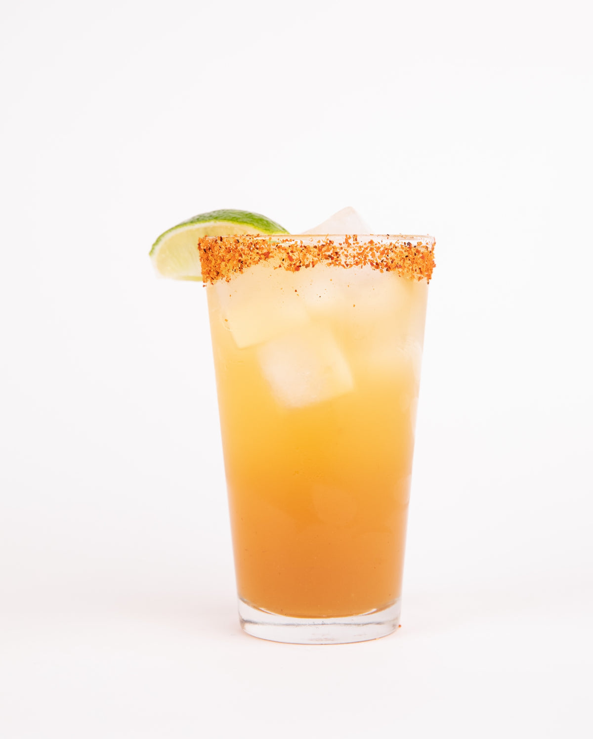Cocktail Crate Sriracha Margarita cocktail in a tall glass with a chili-salt rim and lime wedge on a white backdrop